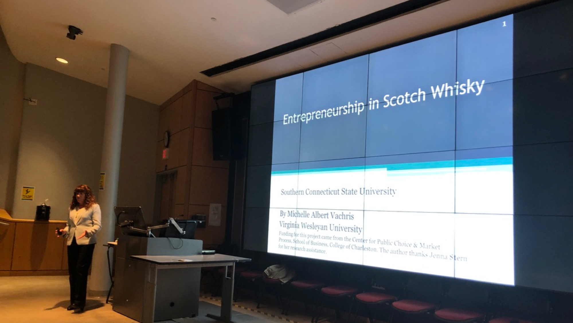 Woman standing in front of presentation which reads "Entrepreneurship in Scotch Whiskey"